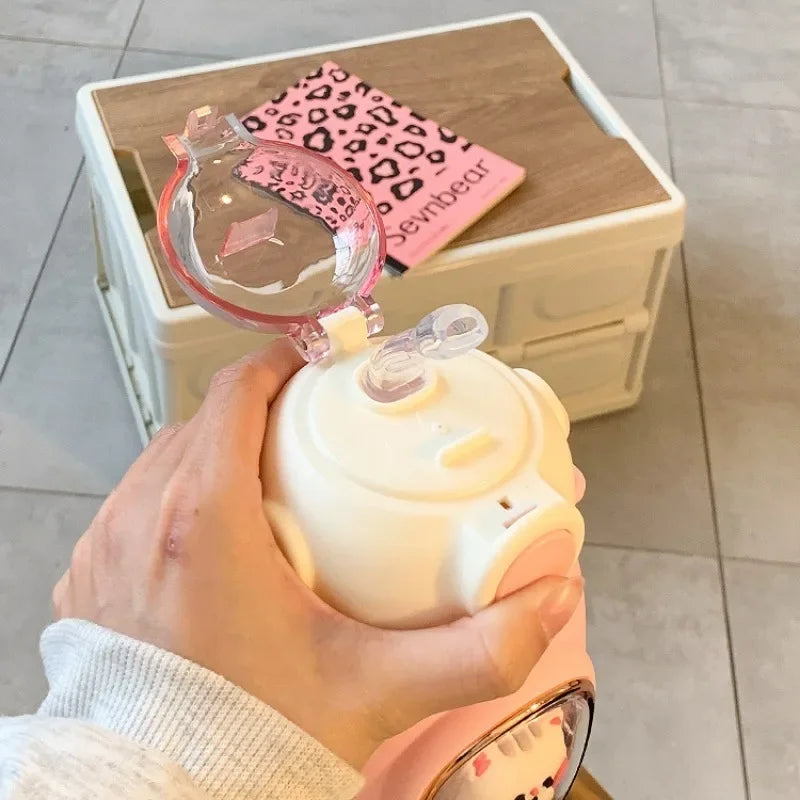 Merit Sell kids water bottle with straw in cream and pink held in hand with transparent lid open
