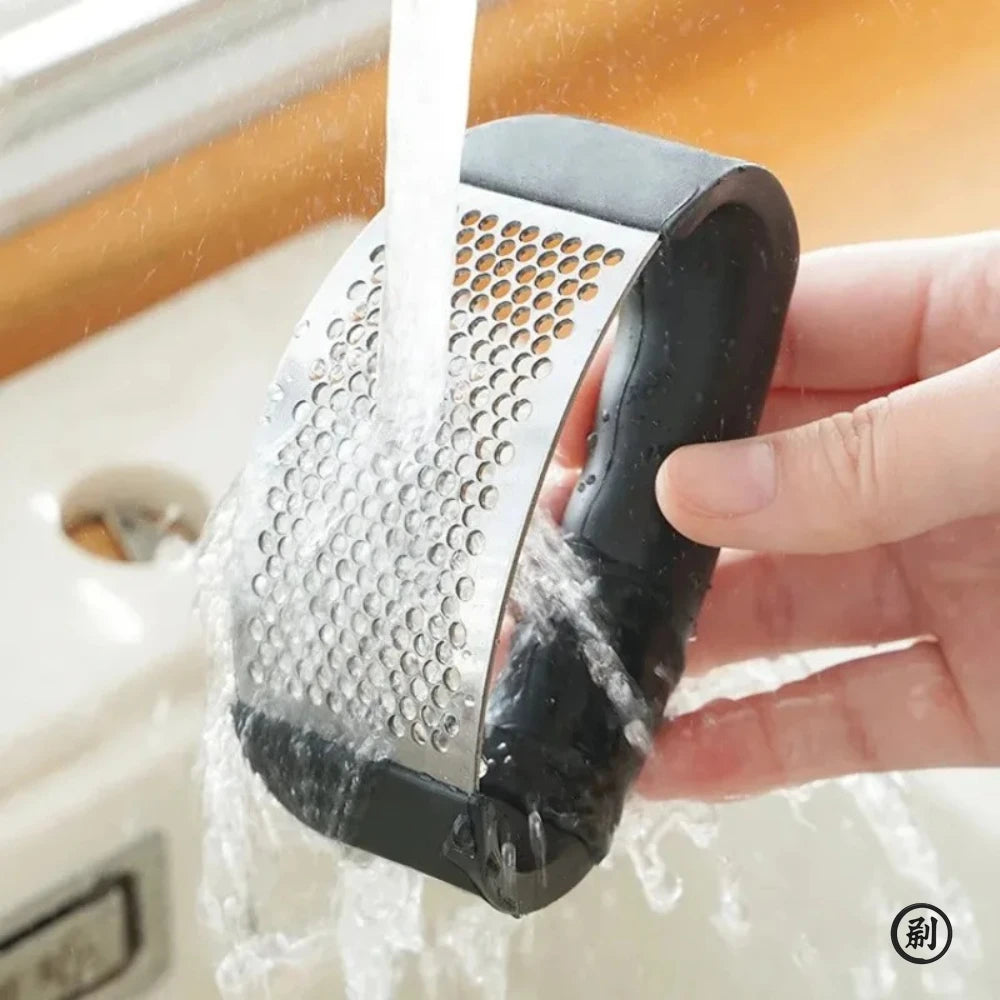 Merit Sell stainless steel garlic press being rinsed under running water for easy cleaning